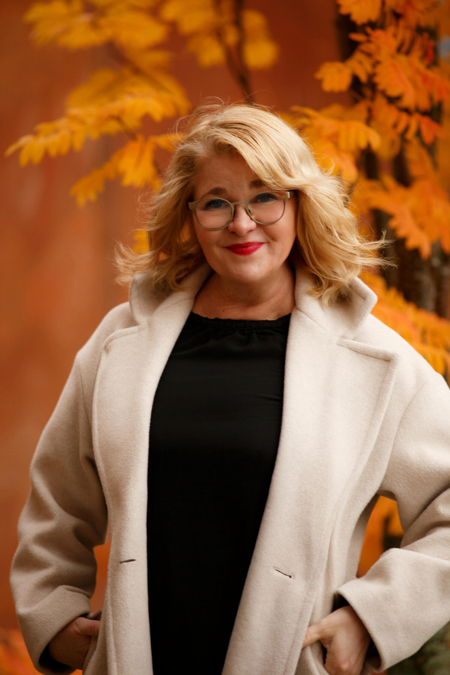 Nainen katsoo kameraan ja hymyilee. Hänellä on vaaleat hiukset ja tumma kauluspaita.